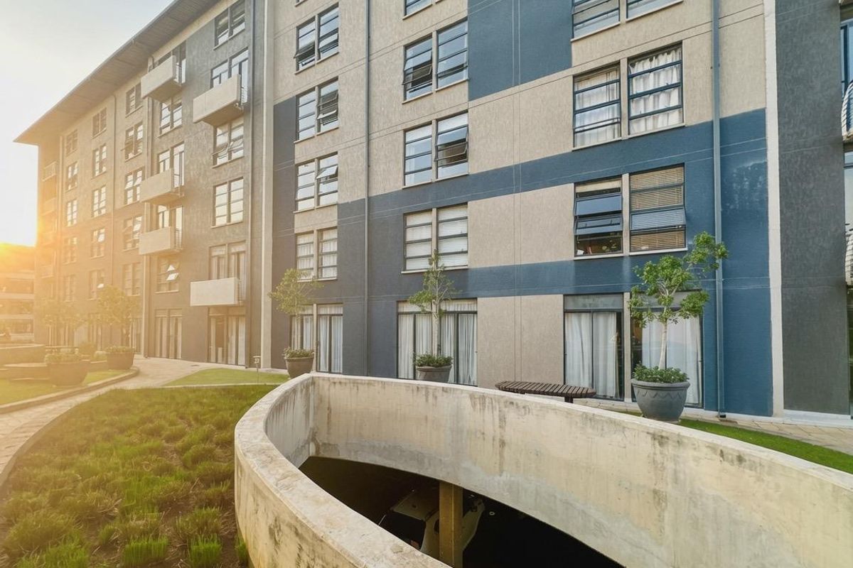 Exterior view of a modern apartment complex featuring a concrete ramp, landscaped garden areas, and multiple levels of balconies.