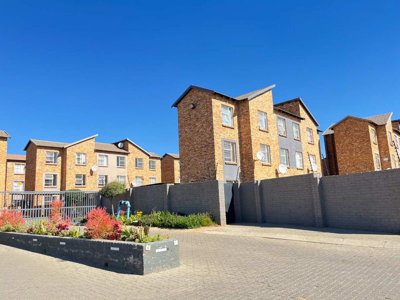 Exterior view of a multi-story apartment complex featuring face brick facades, a secure perimeter wall, and a paved entrance area.