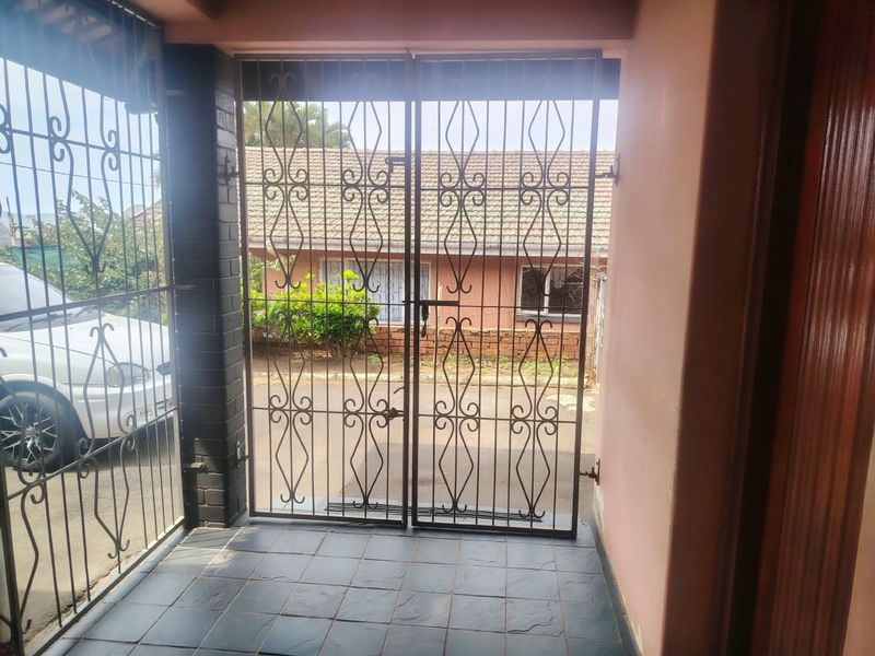 A covered entrance patio featuring tiled flooring and a secure wrought iron gate, providing access to the exterior driveway area.