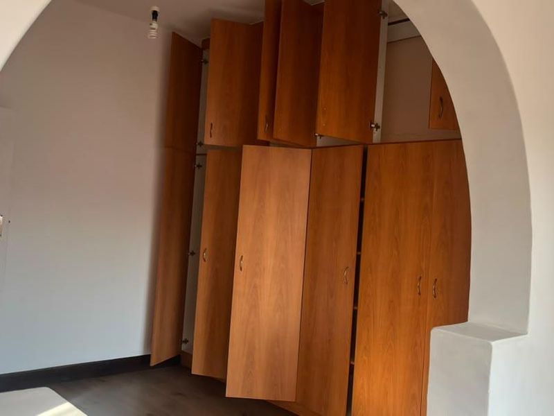A bedroom featuring extensive built-in wooden cabinetry, laminate flooring, and a distinctive arched entryway.