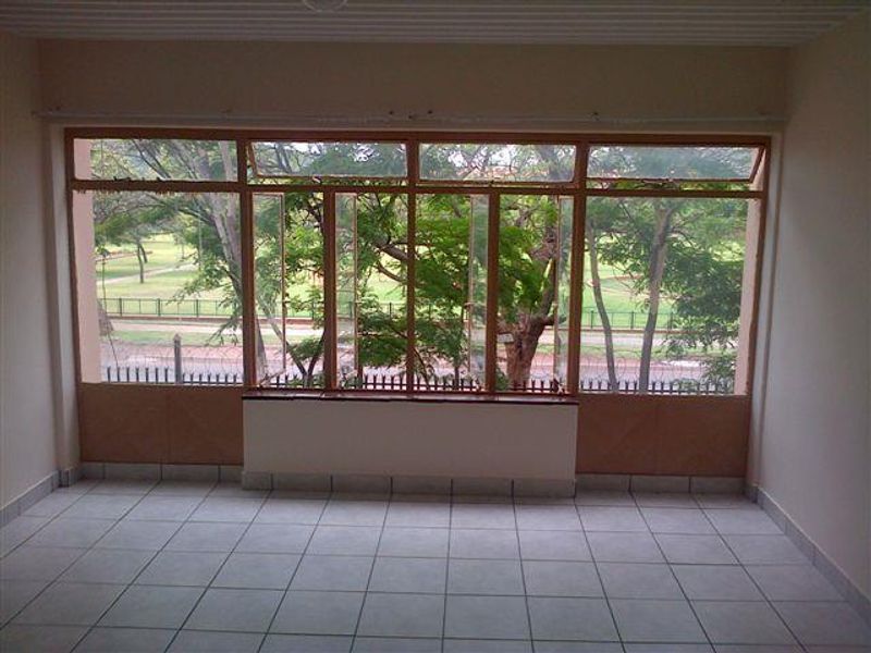 An empty living room featuring large windows with views of the surrounding greenery and tiled flooring throughout.