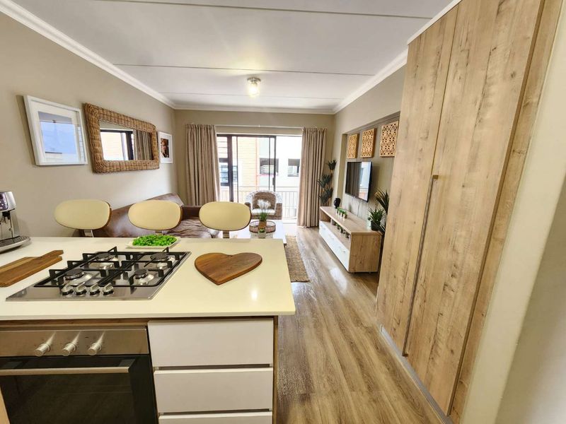 Modern open-plan living area featuring a kitchen island with gas hob, built-in oven, and seamless flow to a private balcony.