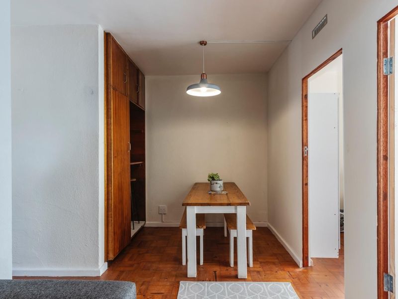 A dining area featuring classic parquet flooring, built-in wooden storage cabinetry, and a modern pendant light fixture, creating a warm and functional space.