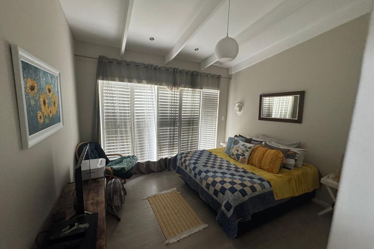 A well-maintained bedroom featuring exposed ceiling beams, plantation shutters, and light-toned wood-look flooring.