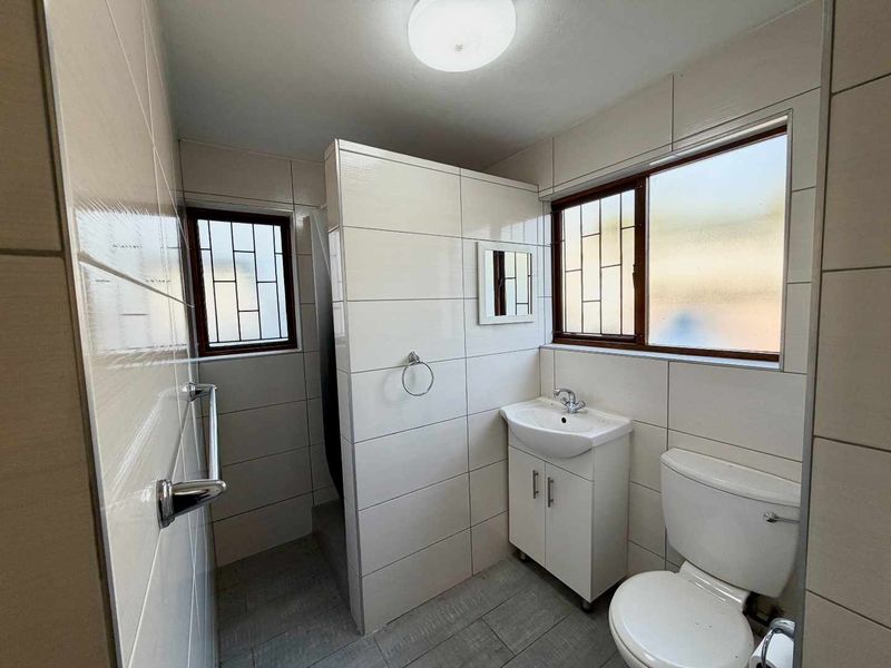 A clean, functional bathroom featuring tiled walls and flooring, a vanity cabinet with a basin, a toilet, and a separate shower area.