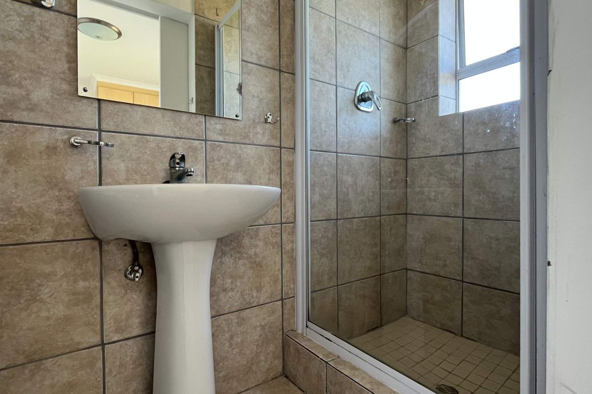A functional bathroom featuring a pedestal basin, tiled walls, and a glass-enclosed shower unit.