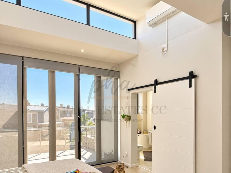 Modern bedroom featuring high ceilings with clerestory windows, floor-to-ceiling sliding doors leading to a balcony, and a contemporary sliding barn door to the ensuite.