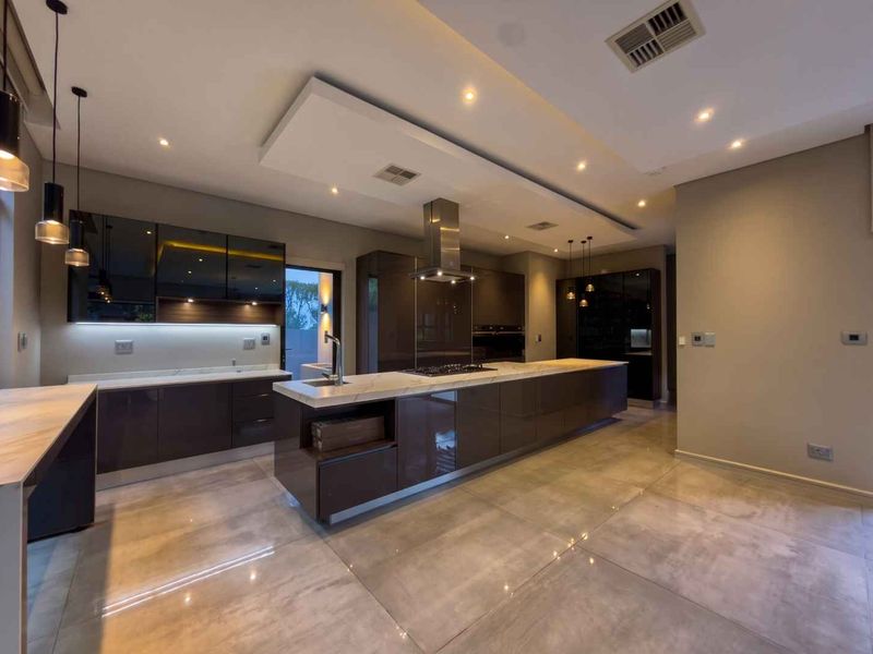 Modern, high-end kitchen featuring a large central island, sleek dark cabinetry, stone countertops, and integrated appliances with recessed lighting.