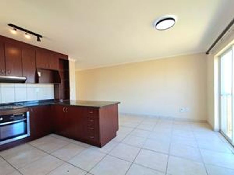Open-plan kitchen and living area featuring dark wood cabinetry, granite countertops, built-in oven, and tiled flooring with access to a balcony.