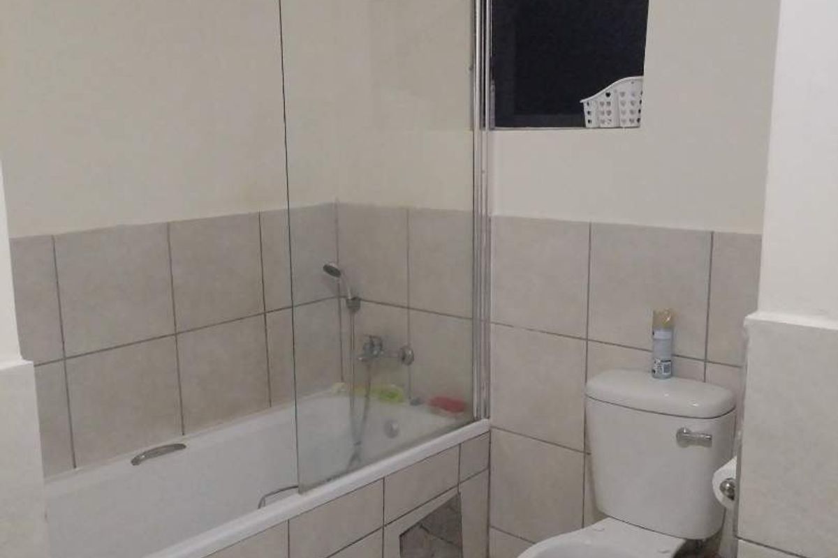 A functional bathroom featuring a bathtub with a glass shower screen, a toilet, and neutral tiled finishes throughout.