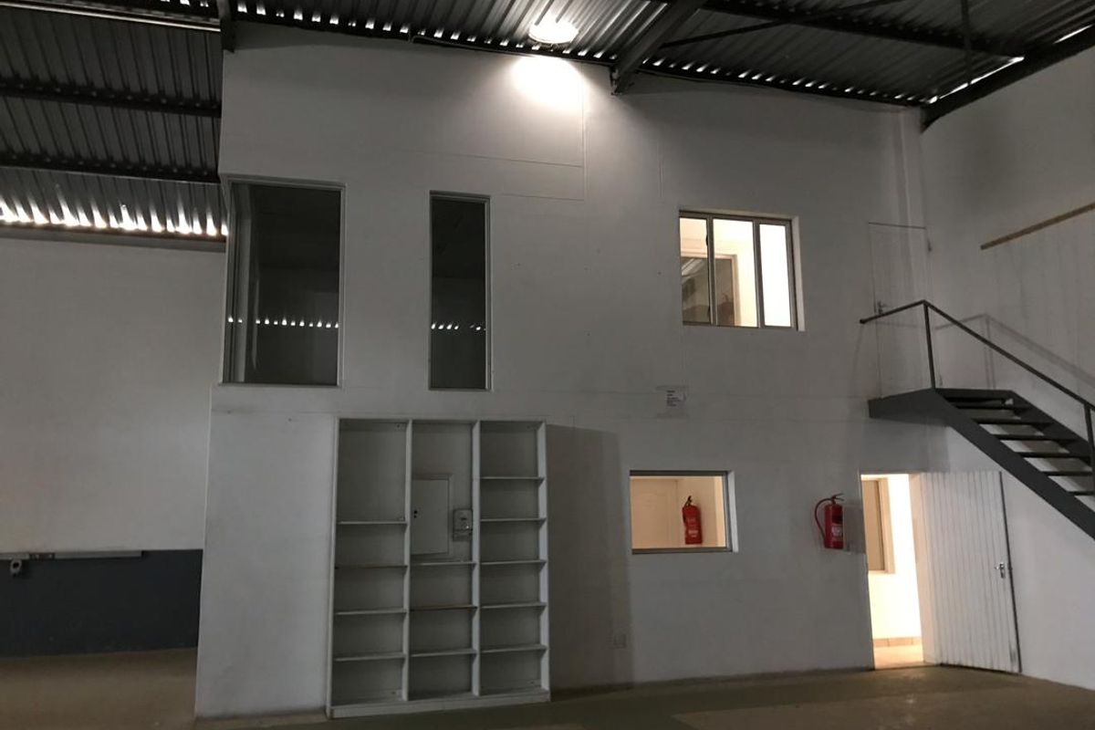 Industrial warehouse interior featuring a steel staircase, built-in shelving, and mezzanine-level office windows under a high corrugated metal roof.