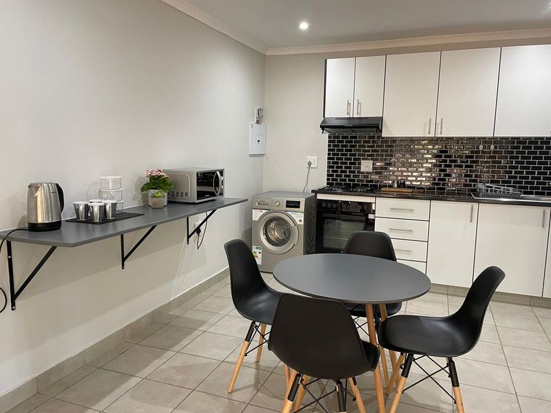 A modern, compact kitchen featuring white cabinetry, a dark subway tile backsplash, integrated appliances, and a functional wall-mounted breakfast bar.