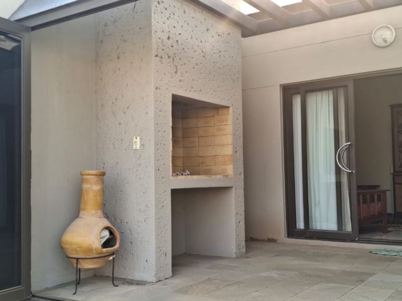 Covered patio area featuring a built-in braai, stone tile flooring, and seamless access to the interior through sliding and folding glass doors.