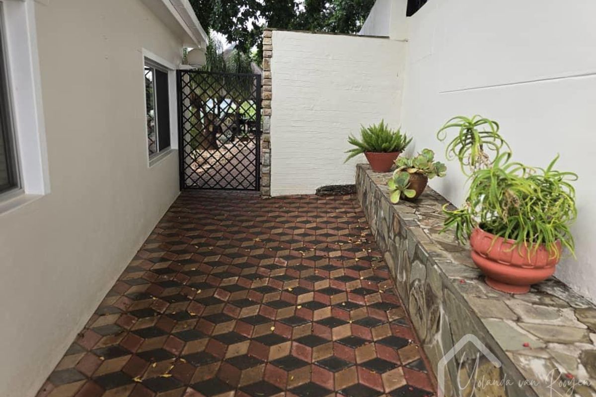 A side walkway or courtyard area featuring patterned paving, a stone-clad retaining wall, and a secure metal gate leading to the rear garden.