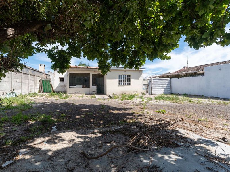Rear exterior view of the property featuring a large yard area, concrete boundary walls, and a small storage structure.