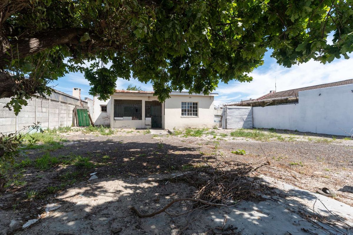 Rear exterior view of the property featuring a large yard area, concrete boundary walls, and a small storage structure.