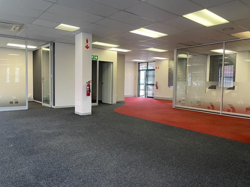 Spacious open-plan office area featuring glass partitioned rooms, suspended ceilings with recessed lighting, and dual-tone carpet flooring.