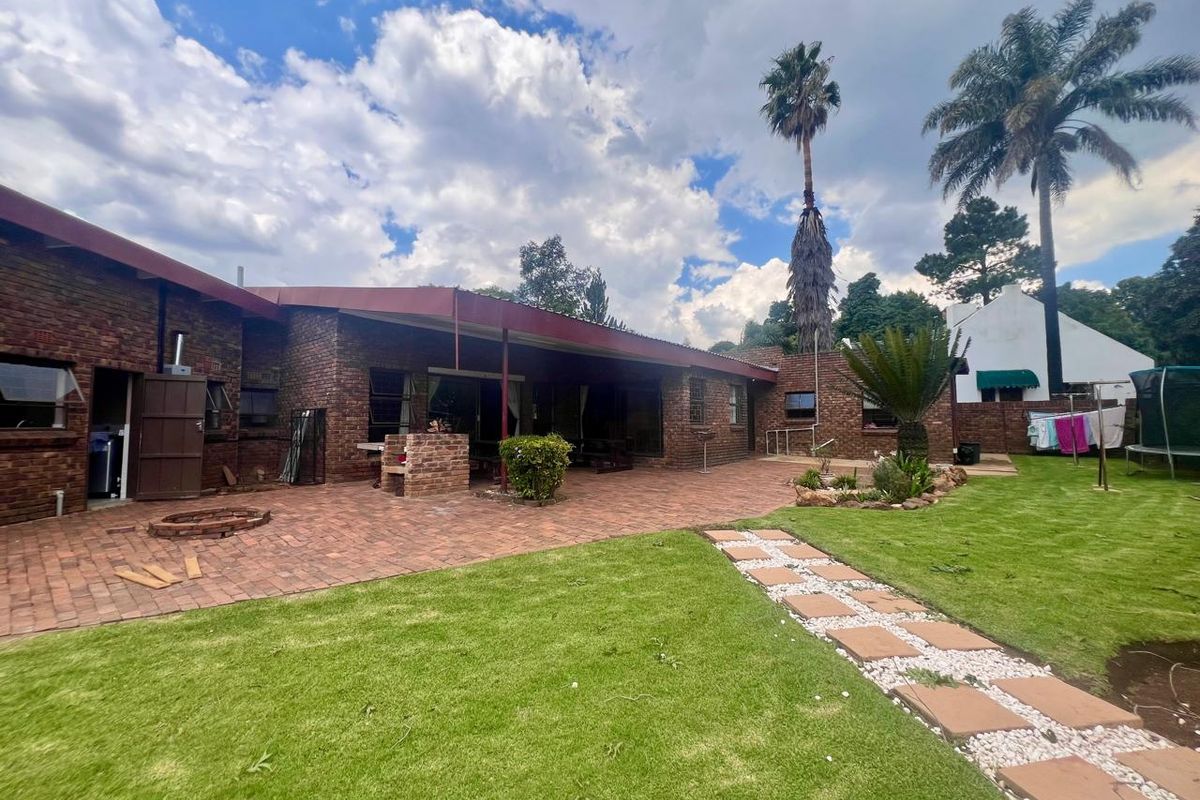 Spacious rear exterior featuring a large brick-paved patio area, built-in brick braai, and a well-maintained garden with established landscaping.
