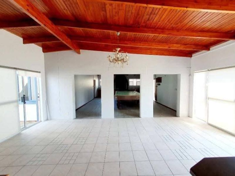 Spacious living area featuring a high exposed timber beam ceiling, tiled flooring, and large sliding glass doors providing ample natural light.