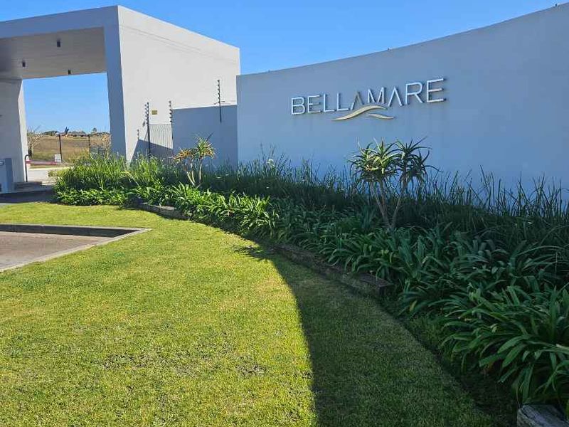 The entrance to Bellamare apartment complex featuring a modern boundary wall, signage, and well-maintained landscaped gardens.