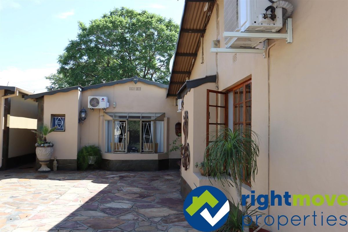 Rear exterior view of the guest house featuring a stone-paved courtyard, bay window, and wall-mounted air conditioning units.