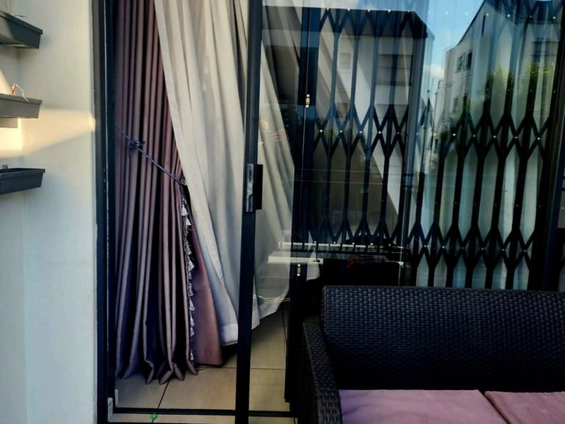A covered balcony area featuring tiled flooring, a sliding glass door with a security gate, and wall-mounted shelving.