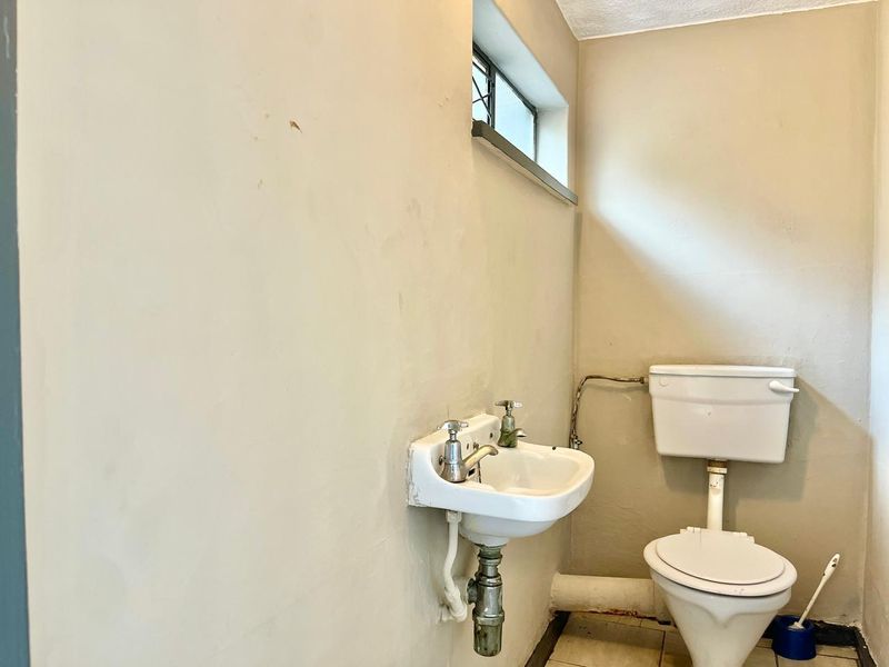 A compact bathroom featuring a wall-mounted basin and standard toilet, requiring cosmetic updates to improve the overall condition and aesthetic appeal.
