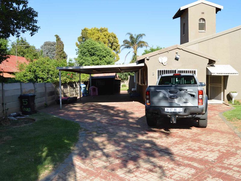 Front exterior view of the property featuring a paved driveway, a covered carport, and secure boundary walling.