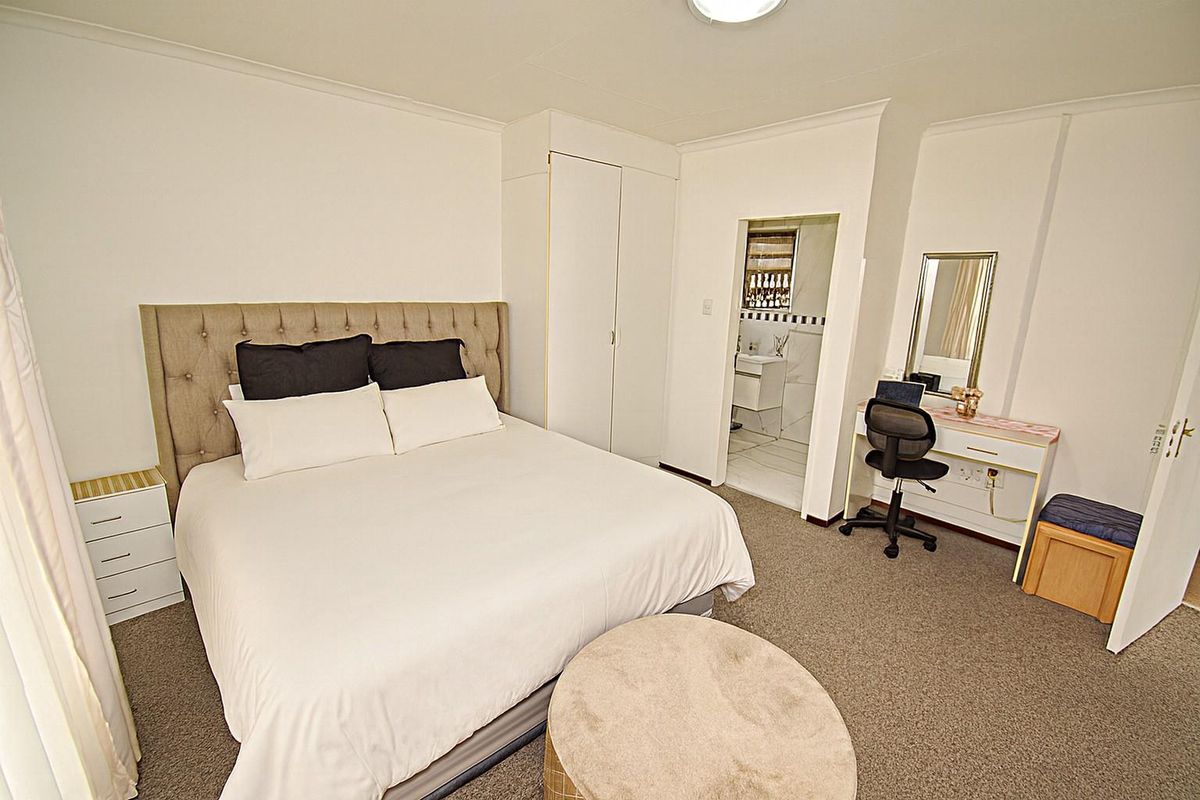 A well-lit bedroom featuring neutral carpeting, built-in wardrobe storage, and an adjoining en-suite bathroom.