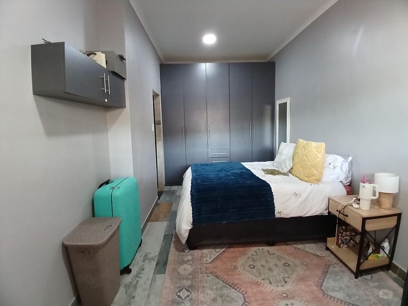 A well-maintained bedroom featuring dark grey built-in cupboards, modern laminate flooring, and recessed ceiling lighting.
