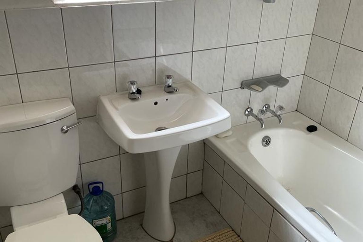 A functional bathroom featuring a pedestal basin, standard toilet, and a bathtub with tiled surround and wall-mounted fixtures.