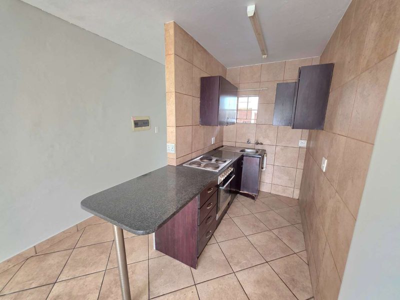 A compact kitchen featuring tiled walls and flooring, built-in cabinetry, an electric hob, and an oven, offering a functional space ready for updates.