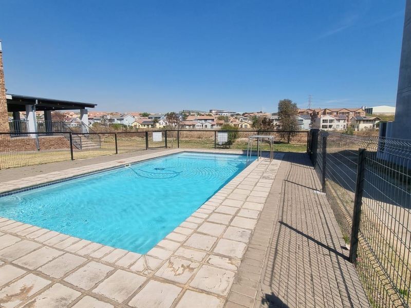 A communal swimming pool area featuring paved surrounds and secure metal perimeter fencing, set within a residential apartment complex.