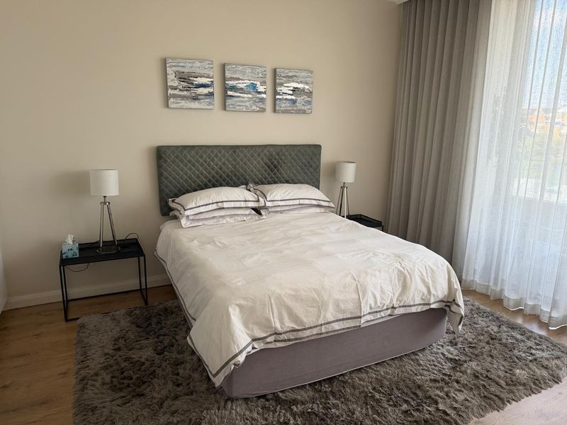 A well-maintained bedroom featuring neutral wall tones, laminate flooring, and floor-to-ceiling curtains providing ample natural light.