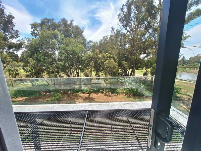 A modern balcony featuring a sleek glass balustrade and metal grid flooring, offering scenic views of the surrounding trees and landscape.