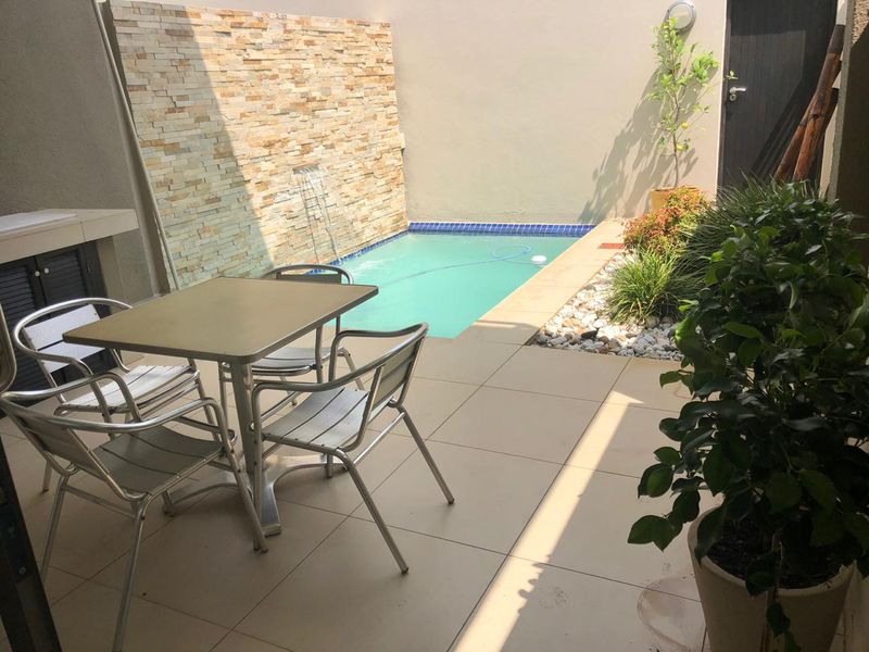 A private courtyard featuring a swimming pool, a decorative stone feature wall, and a tiled patio area suitable for outdoor dining.