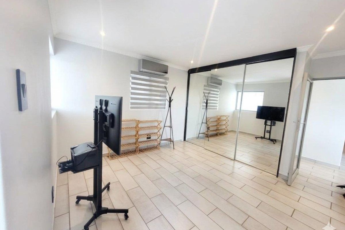 A bright, spacious bedroom featuring large mirrored sliding wardrobes, tiled flooring, and a wall-mounted air conditioning unit.