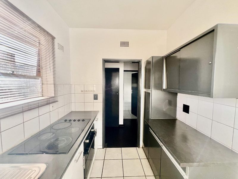 A functional, compact kitchen featuring built-in cabinetry, an electric hob, oven, and tiled splashbacks, offering a clean space ready for modernization.