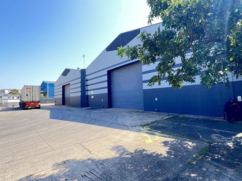 Industrial warehouse exterior featuring large roller shutter doors, metal cladding, and a spacious concrete yard area suitable for logistics and heavy vehicle access.