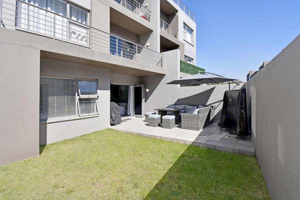 A private rear garden featuring a paved patio area, lawn, and direct access to the apartment via sliding doors.