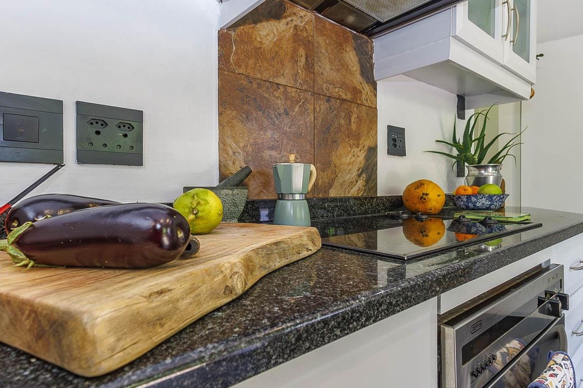 A functional kitchen workspace featuring dark granite countertops, a built-in oven, a glass cooktop, and a decorative stone-tiled splashback.
