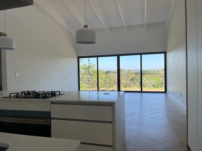 Spacious open-plan living area featuring a modern kitchen island with gas hob, herringbone flooring, vaulted ceilings, and large sliding doors opening to scenic views.