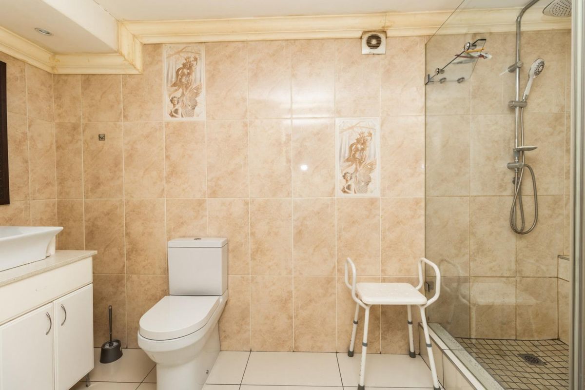 A functional bathroom featuring a walk-in shower with glass enclosure, vanity basin, and toilet, finished with neutral wall and floor tiling.
