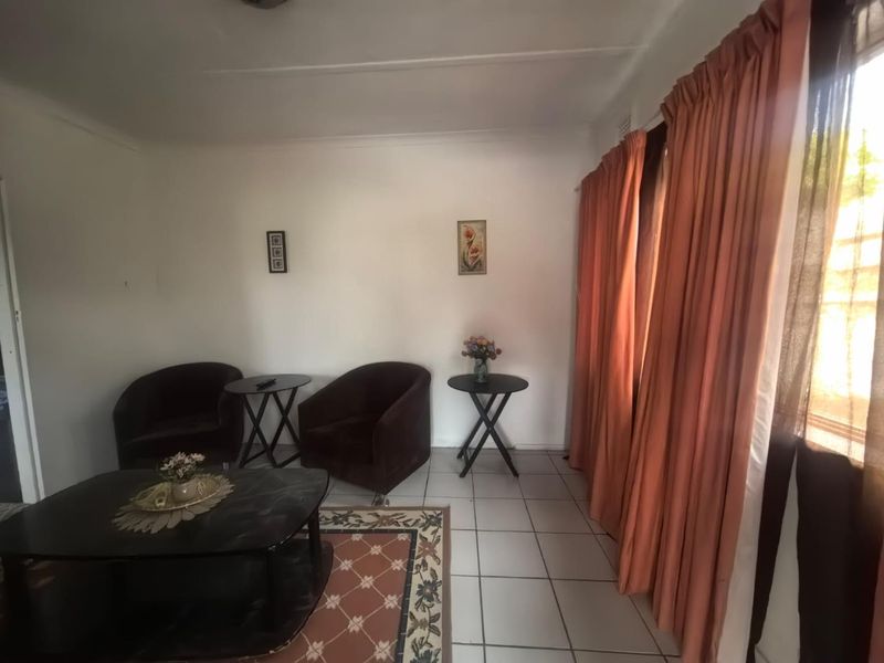 A simple living room featuring neutral tiled flooring and large windows with floor-to-ceiling curtains, offering a functional and well-lit space.