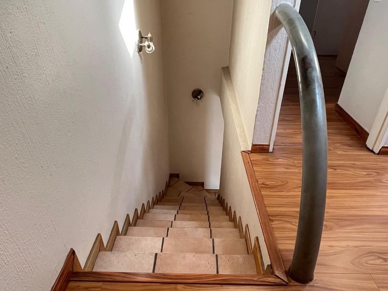 A staircase featuring tiled steps and a curved metal handrail, transitioning from a laminate-floored landing area.