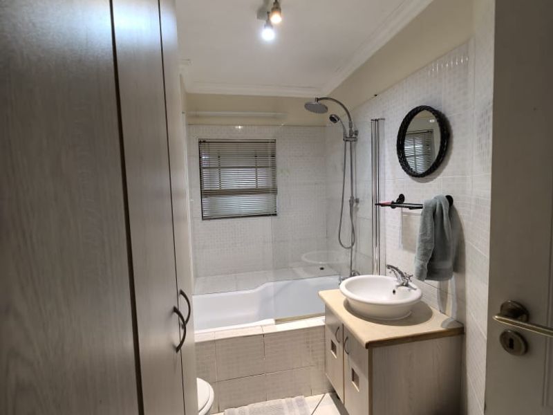 A functional bathroom featuring a shower-over-bath combination, a vessel sink vanity, and built-in storage cupboards with tiled finishes throughout.