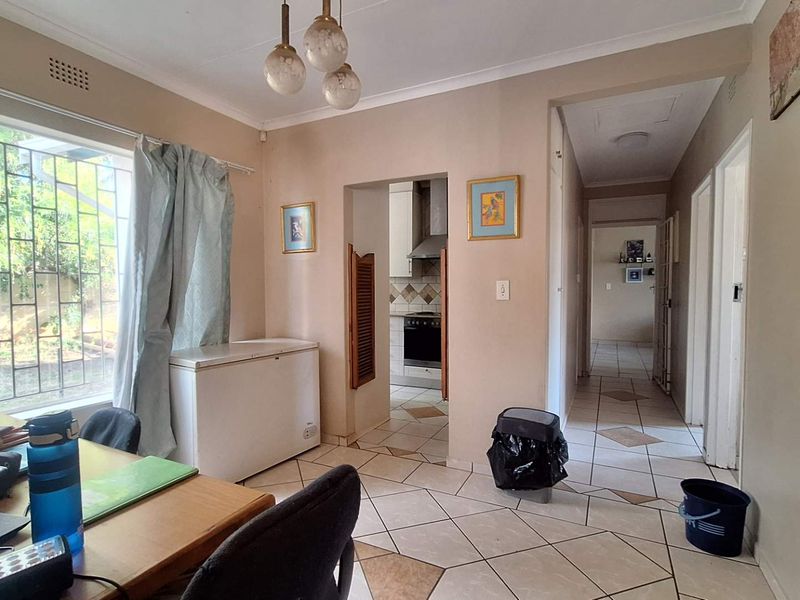 A living area featuring tiled flooring, an archway leading to the kitchen, and large windows with security bars.