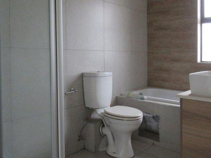 A bathroom featuring a shower, bathtub, toilet, and vanity with a vessel sink. The bathtub panel is currently missing, exposing the plumbing.