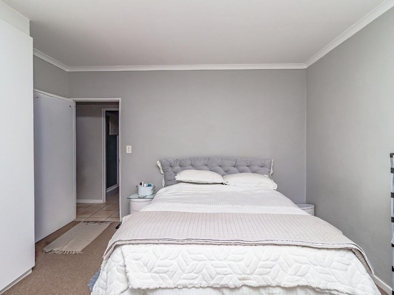 A well-maintained bedroom featuring neutral grey walls, carpeted flooring, and a built-in wardrobe with direct access to an adjoining bathroom.