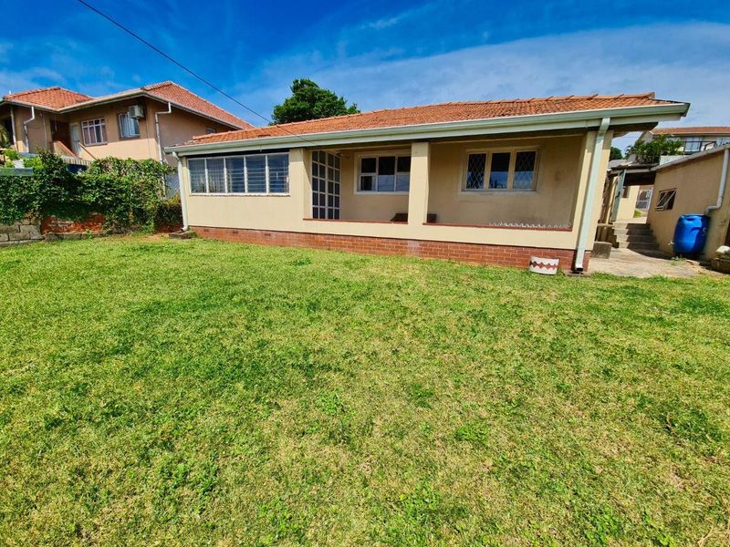 Rear view of the house featuring a covered patio area, terracotta roof tiles, and a spacious lawn.